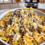 A white bowl filled with cheesy beef bow tie pasta covered in melted cheese and fresh parsley garnish.