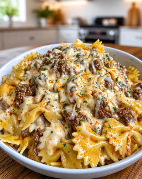 A white bowl filled with cheesy beef bow tie pasta covered in melted cheese and fresh parsley garnish.