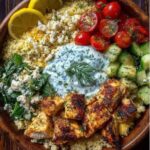 Easy Mediterranean chicken couscous bowl recipe served in a wooden bowl topped with tzatziki, feta, tomatoes, and cucumbers.