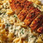Plated creamy garlic parmesan farfalle pasta topped with sliced crispy herb chicken and fresh parsley garnish.