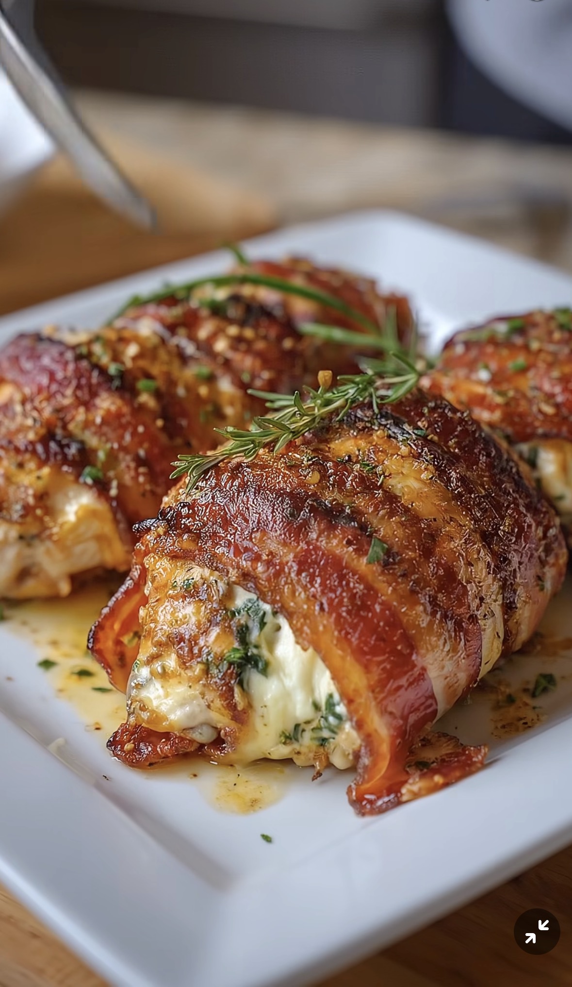 Bacon Wrapped Cream Cheese Stuffed Chicken Breast on a white serving plate with herbs and crispy bacon.