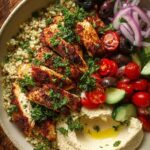 A loaded Mediterranean Chicken Quinoa Bowl featuring spiced grilled chicken, quinoa, sliced tomatoes, cucumbers, and a side of smooth hummus.