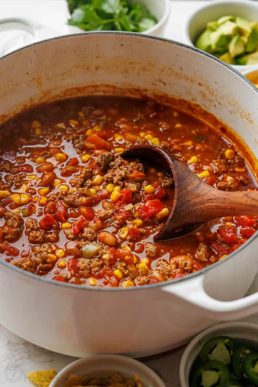 A large white pot filled with a hearty easy taco soup recipe, garnished with fresh cilantro and avocado.